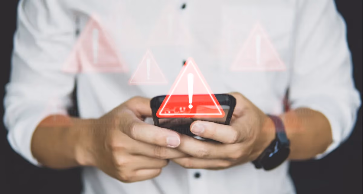 A person holding a phone with a red warning symbol