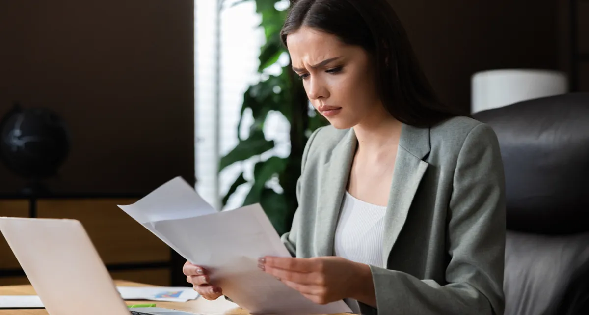 A young lady holding up paperwork in front of her looking confused