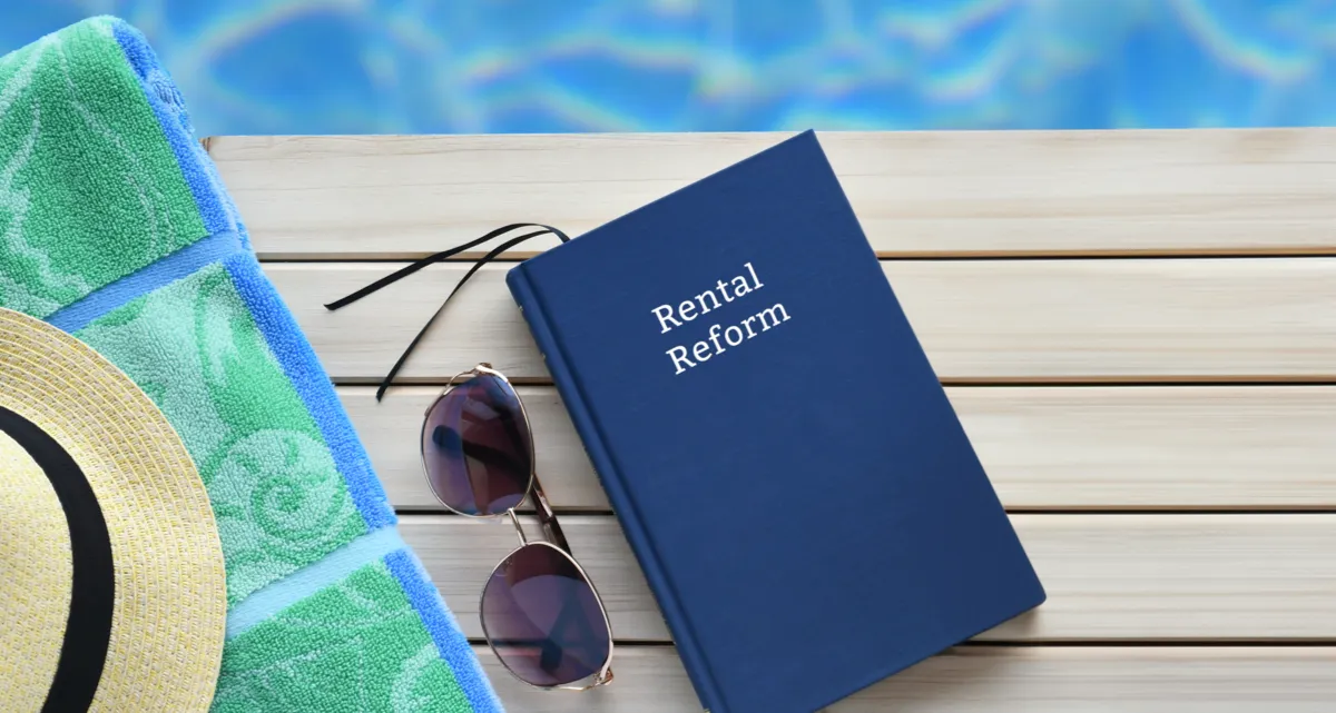 A book titled Rental Reform, sunglasses and a hat on a table by a pool
