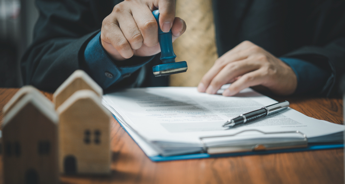 A person stamping a form on a desk next to some model houses