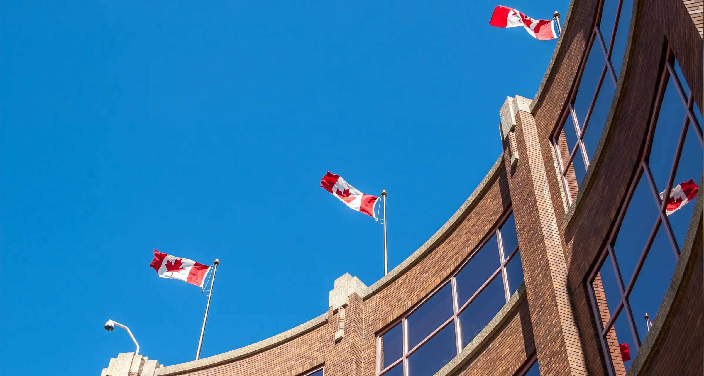 Three Canadian flags flying on poles on top of a building