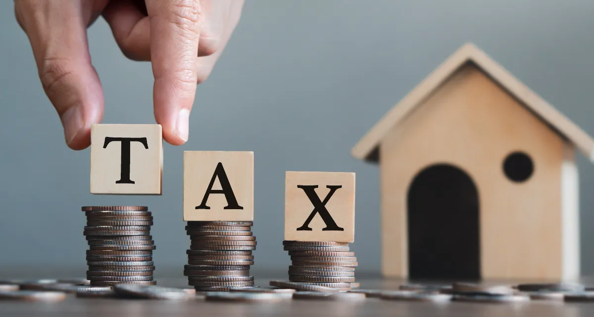 Three stacks of coins next to a model house with letter blocks marked T, A and X being placed on top of them