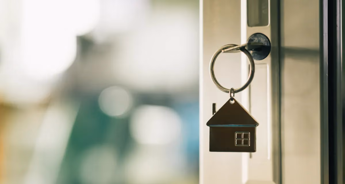 A key with a house-shaped keychain in the lock of an open door