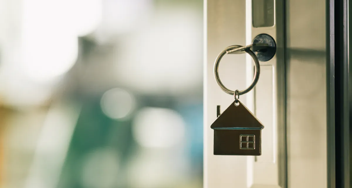 A key with a house-shaped keychain in the lock of an open door
