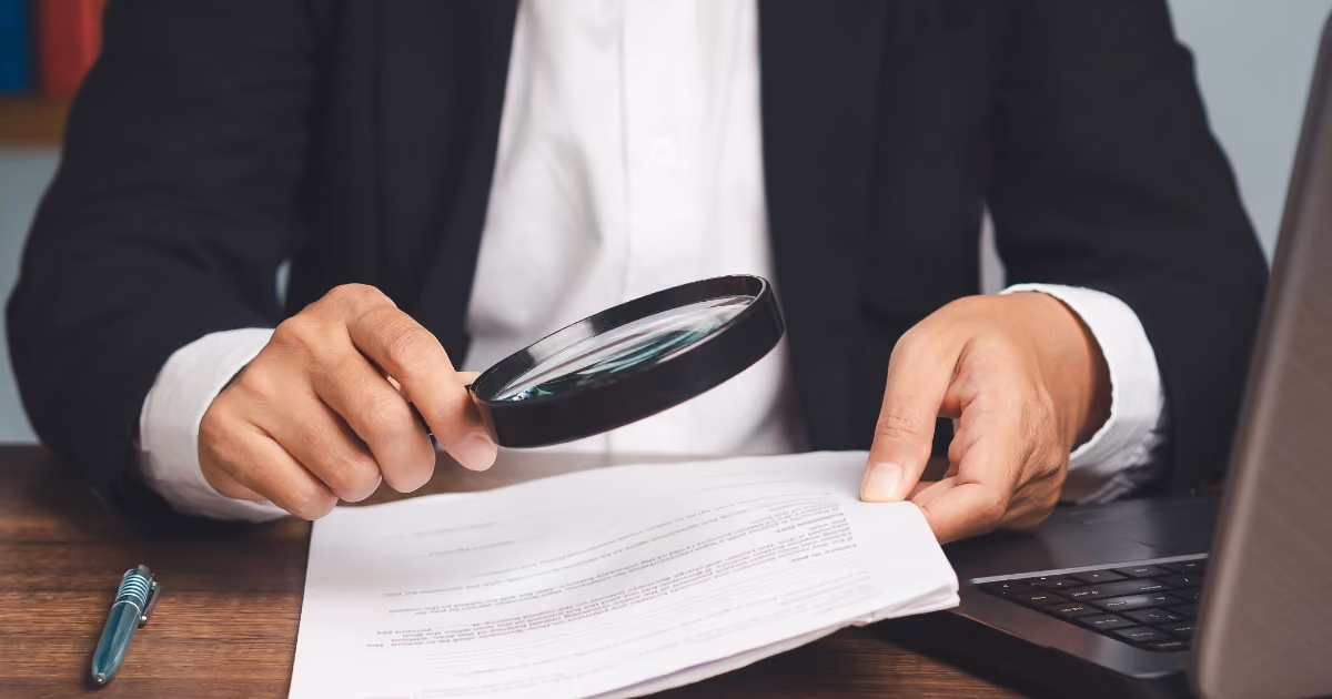 A person looking at documents through a magnifying glass