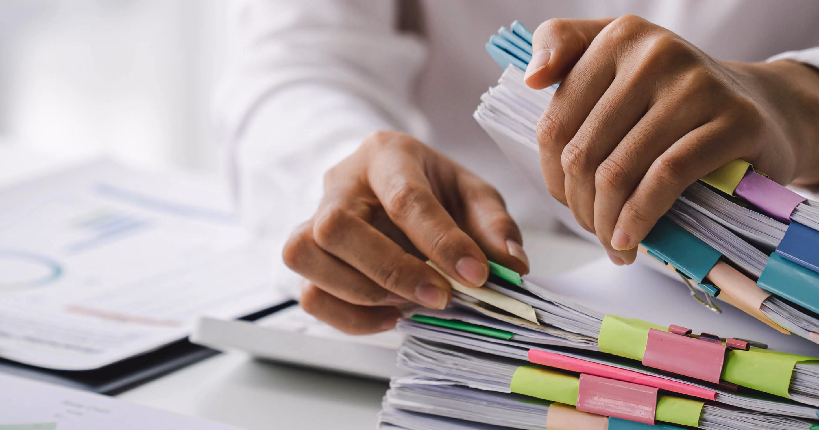 A pair of hands sorting through a pile of papers in binders