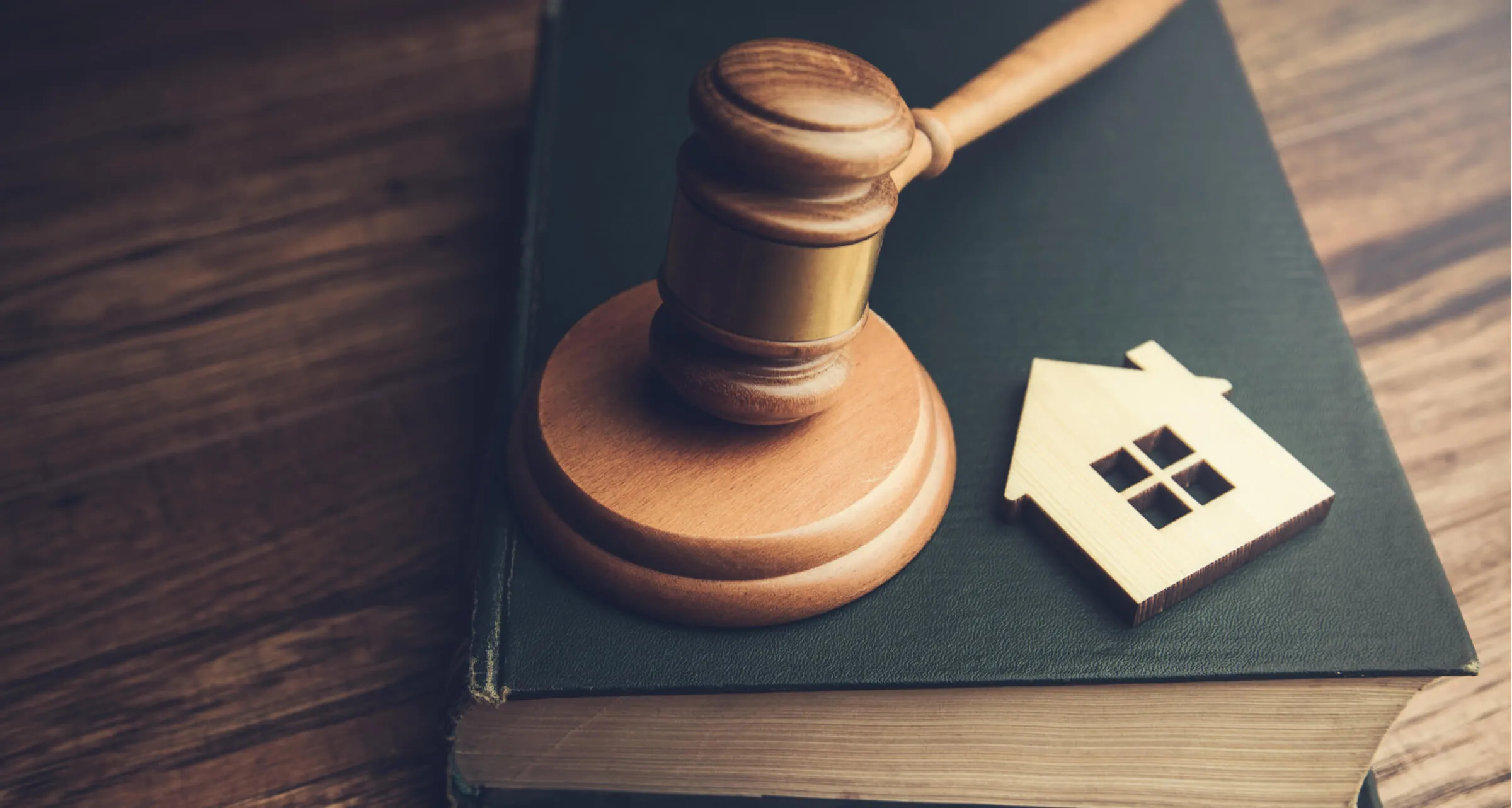 A court room gavel resting on a book and model house
