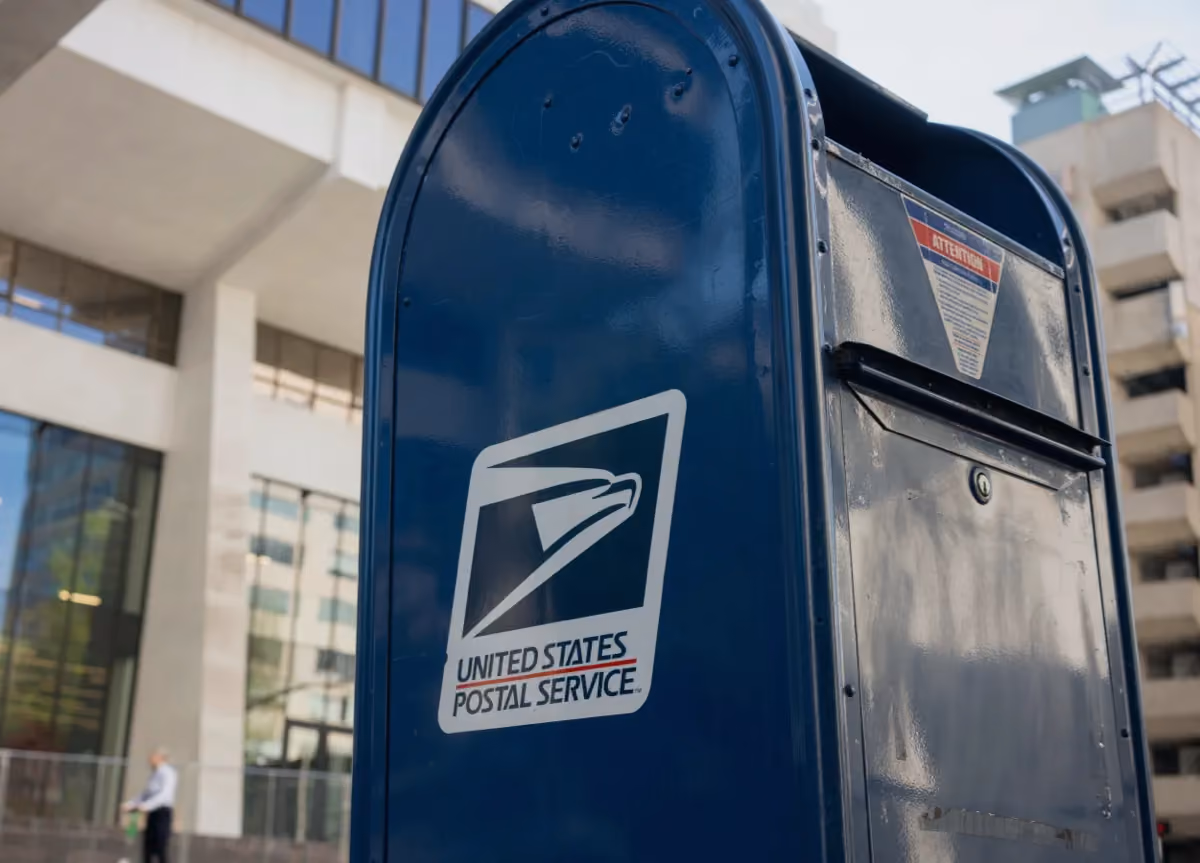 Close-up of a blue USPS mailbox on the street in front of a building