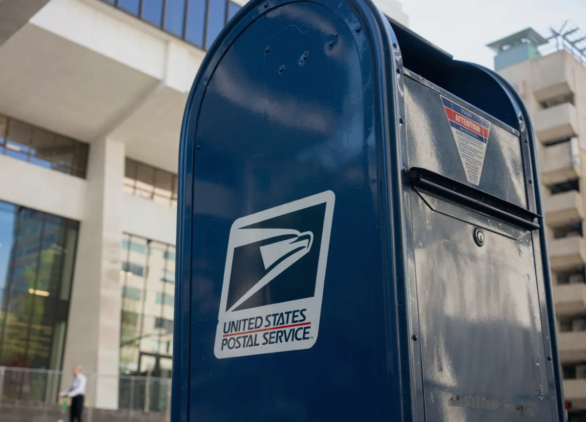 Close-up of a blue USPS mailbox on the street in front of a building