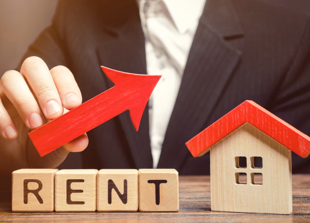 Wooden blocks spelling the word “Rent” next to a wooden house and an upward arrow.