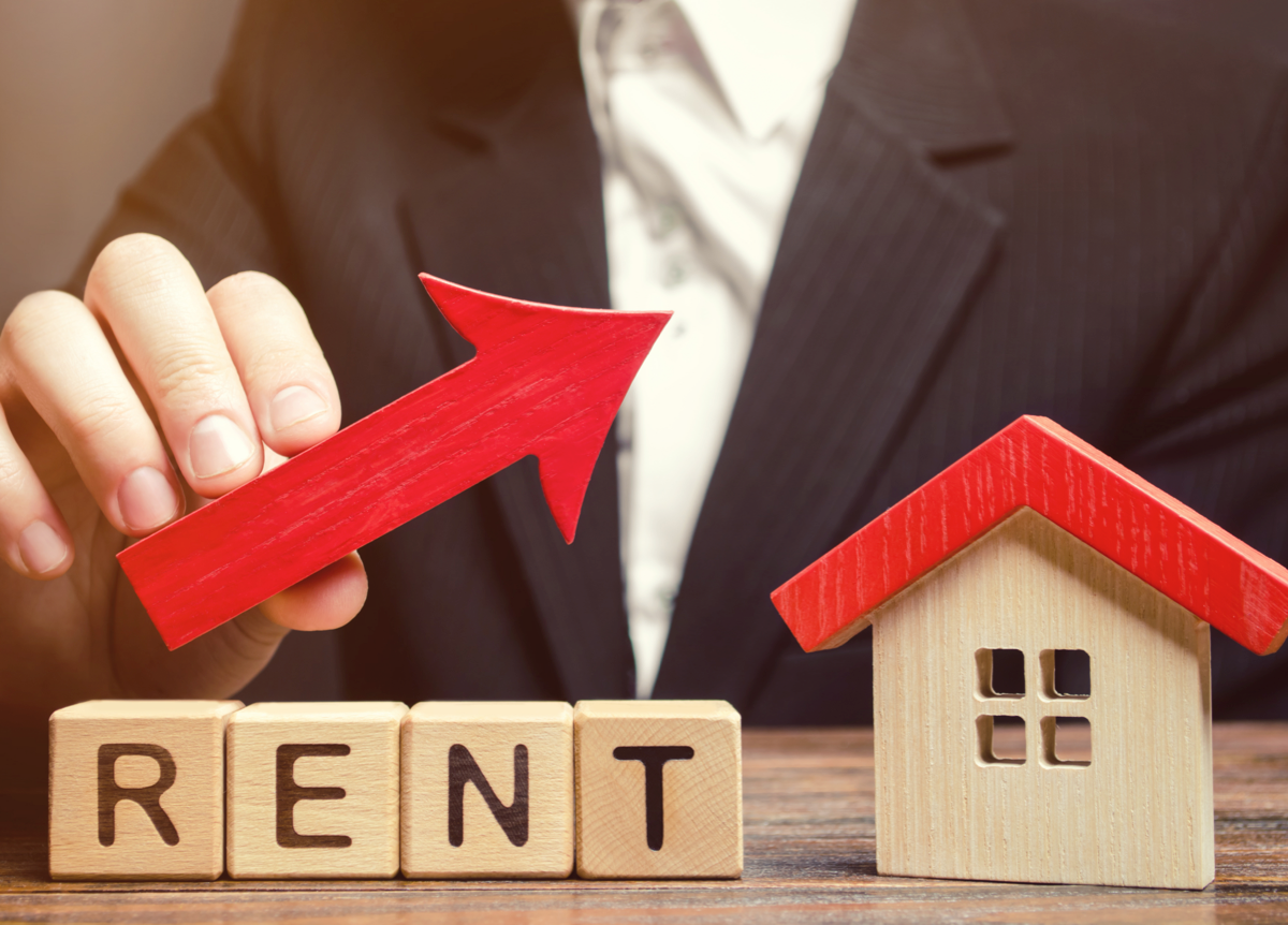 Wooden blocks spelling the word “Rent” next to a wooden house and an upward arrow.
