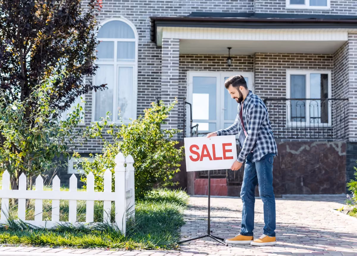 Man putting up 'for sale' sign in front of his house