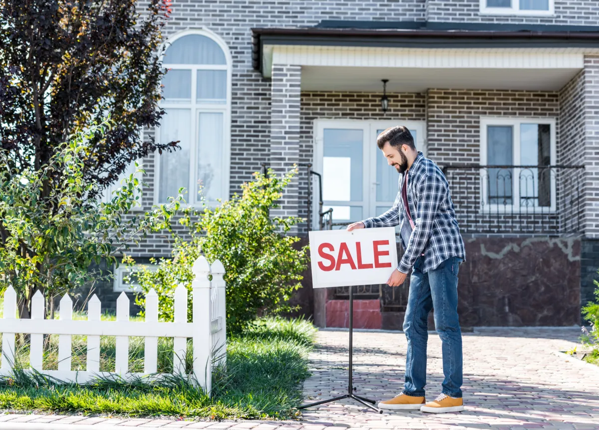 Man putting up 'for sale' sign in front of his house