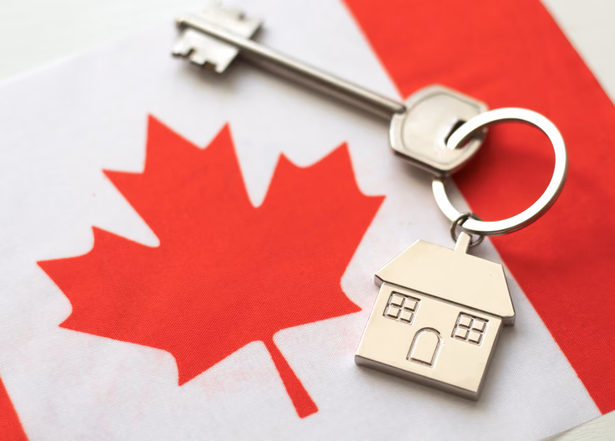 Key with little house keychain on top of Canadian flag