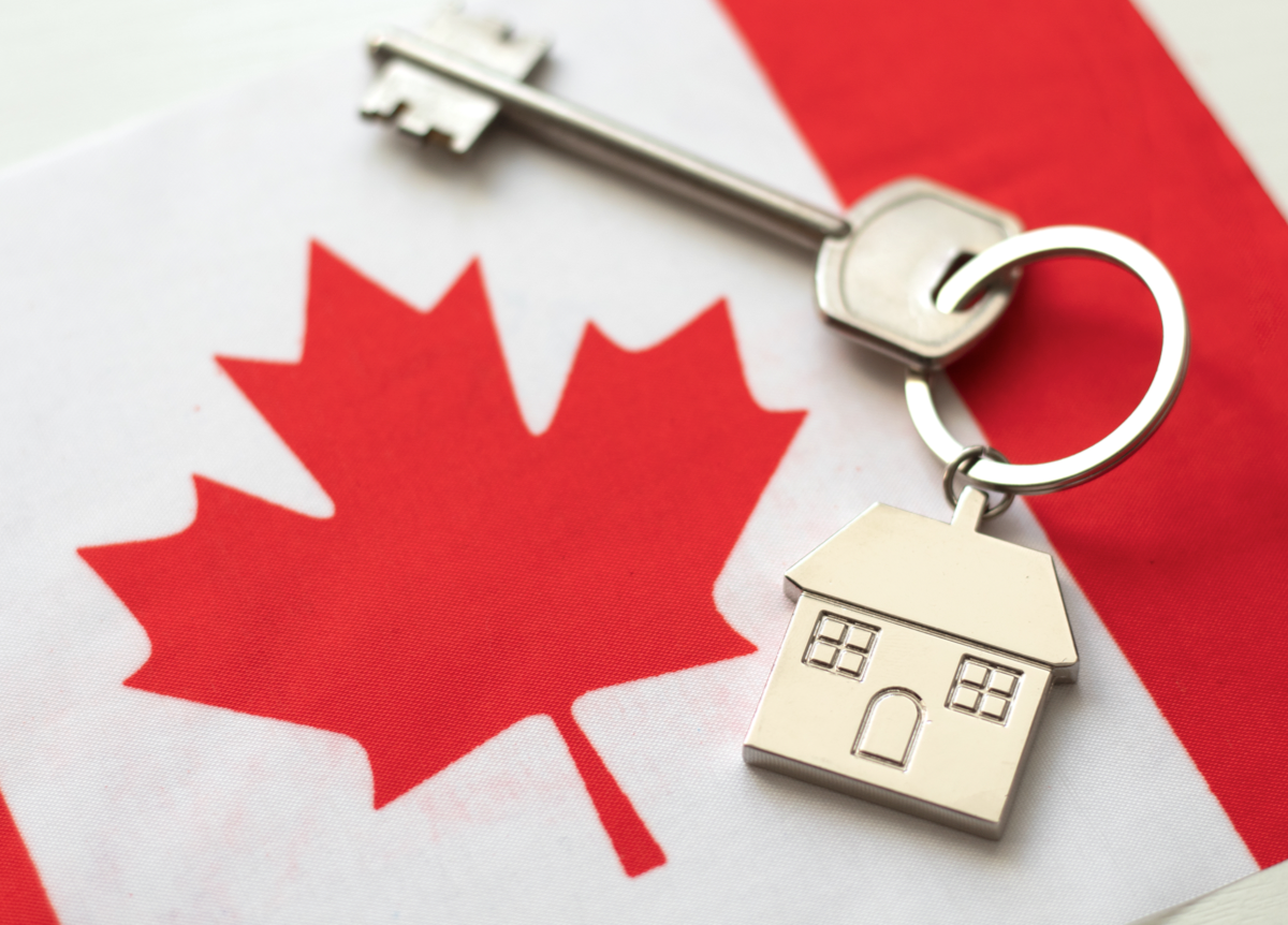 Key with little house keychain on top of Canadian flag
