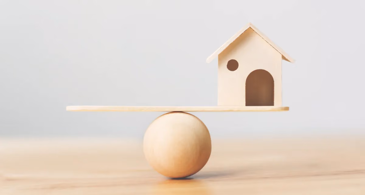 A model house balancing on a plank on a ball