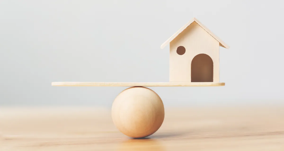 A model house balancing on a plank on a ball