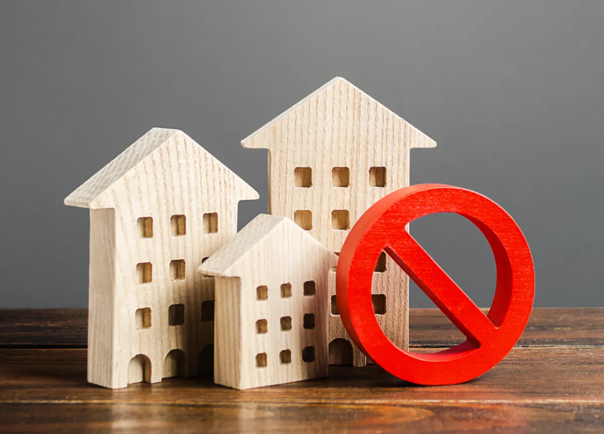 Red prohibition sign in front of three wood models of residential buildings