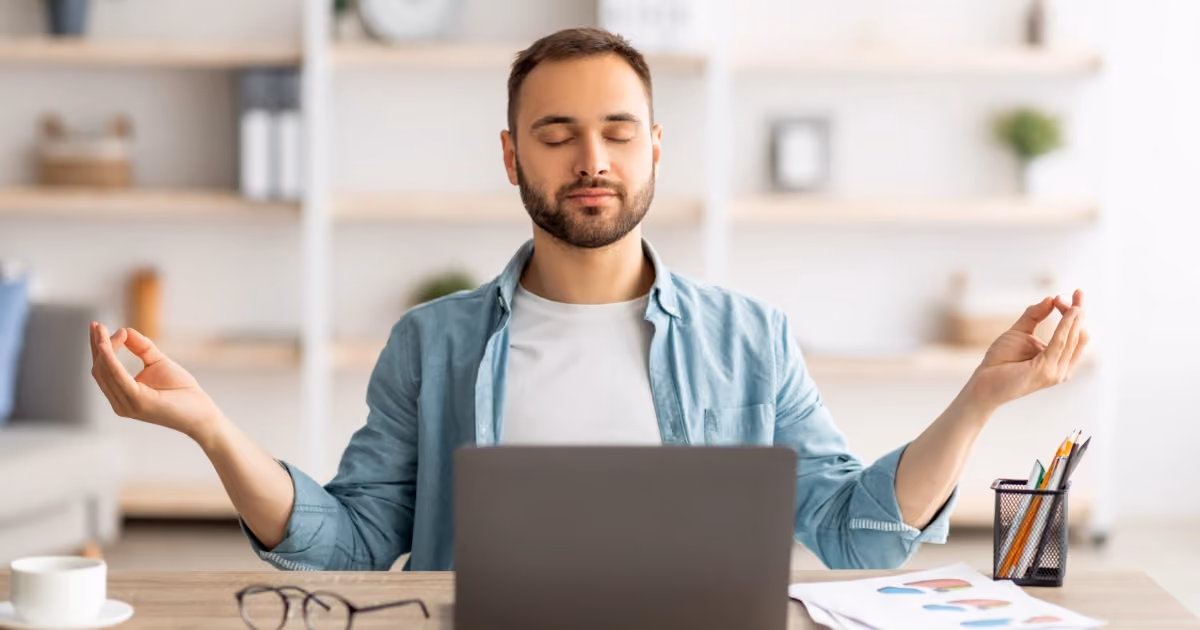 A man in a yoga pose sitting in front of a laptop