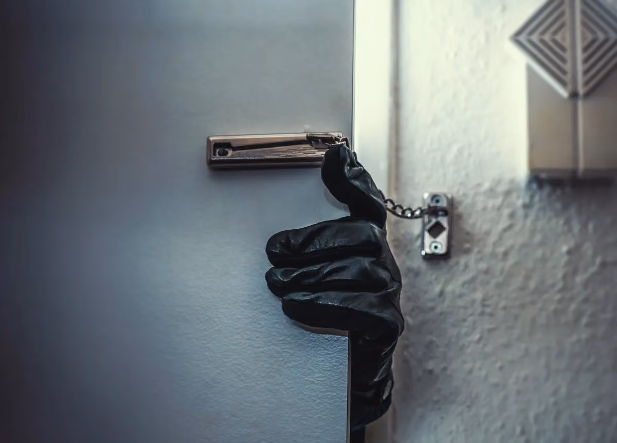 A hand wearing a black glove trying to unchain a door from the outside