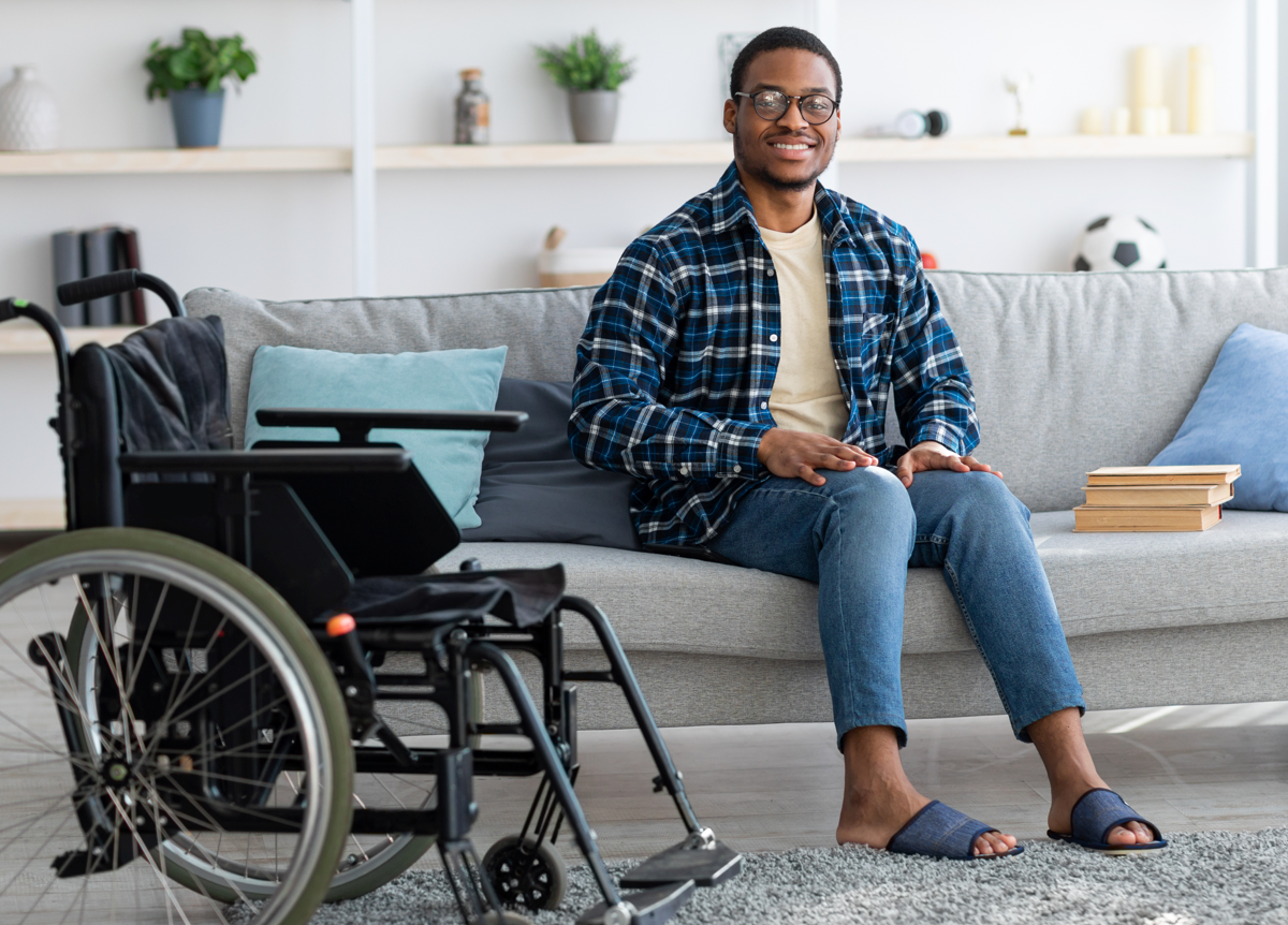 Smiling guy sitting on sofa with a wheelchair next to him
