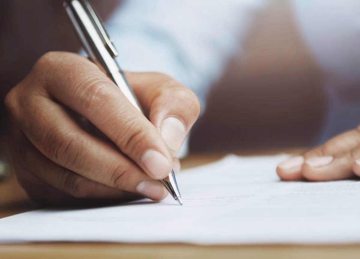 Close-up of hand holding pen and writing on lined paper.