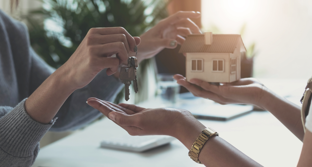 A pair of hands passing a model house and a pair of keys to another pair of hands