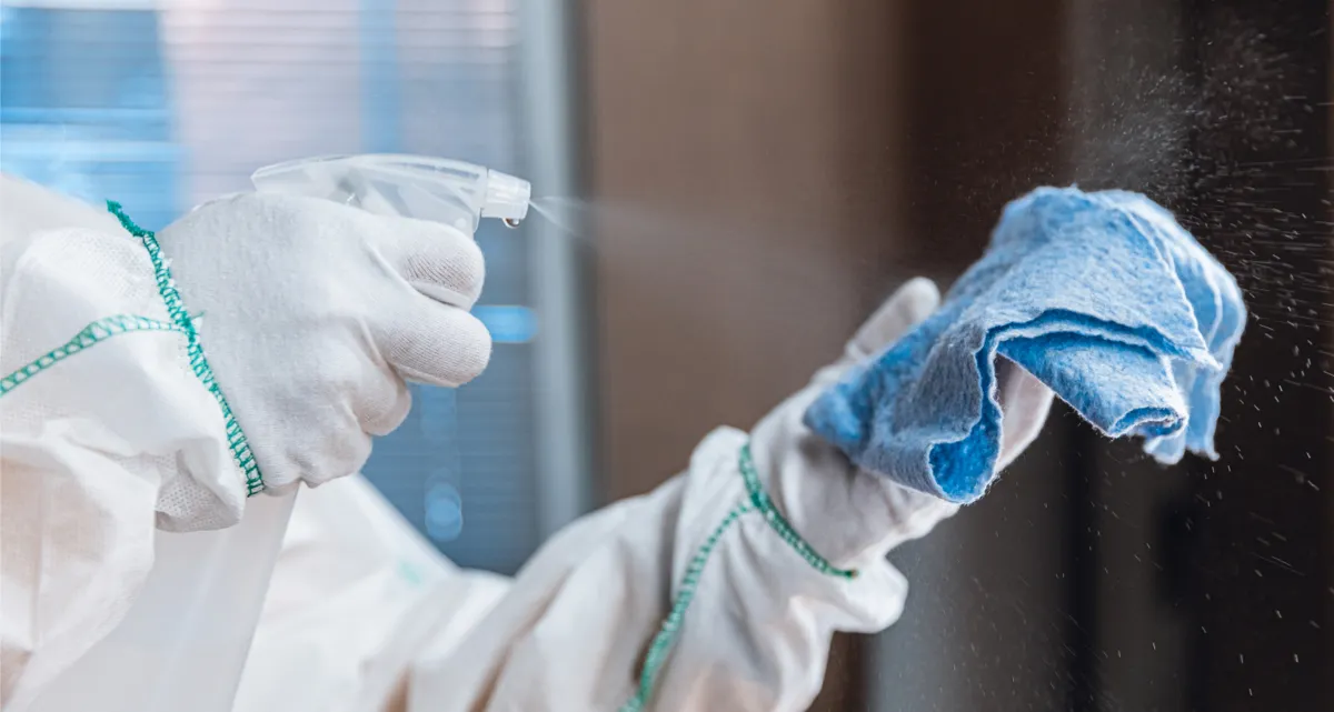 A person wearing gloves and an overshirt spraying a cloth with a spray bottle