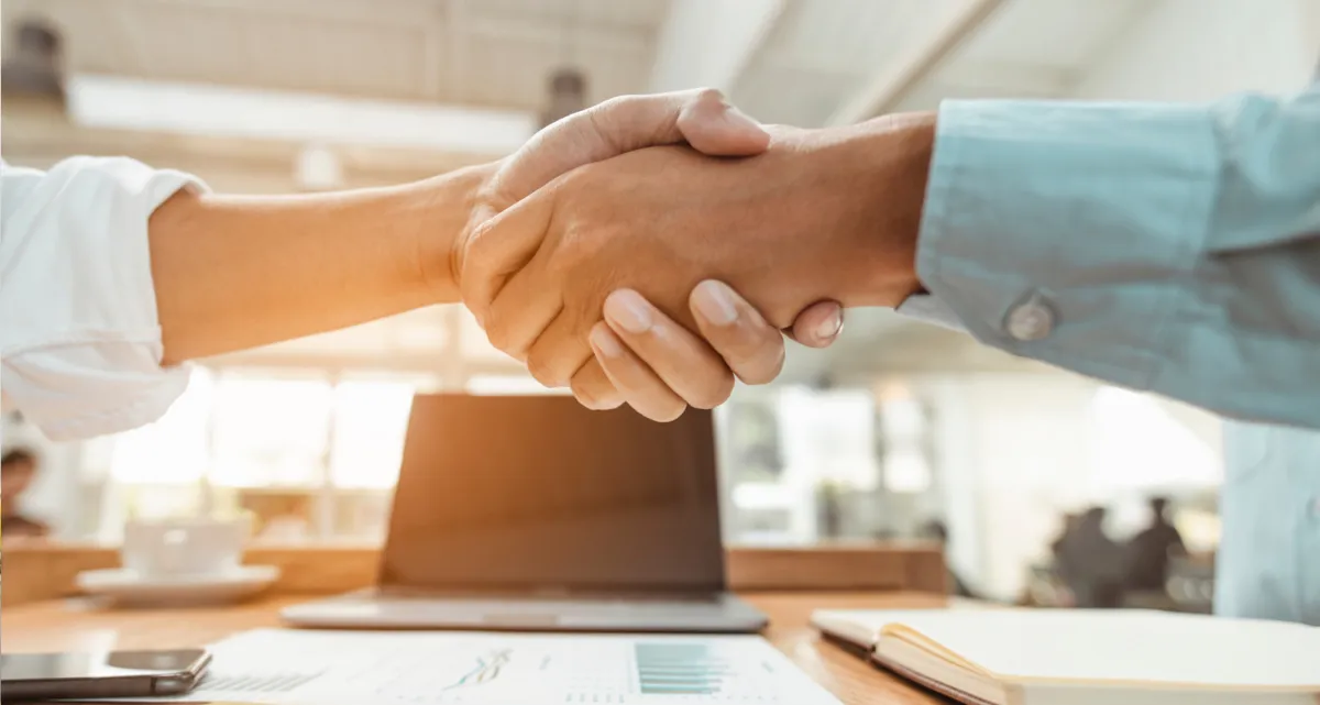 A closeup of a handshake in front of a laptop