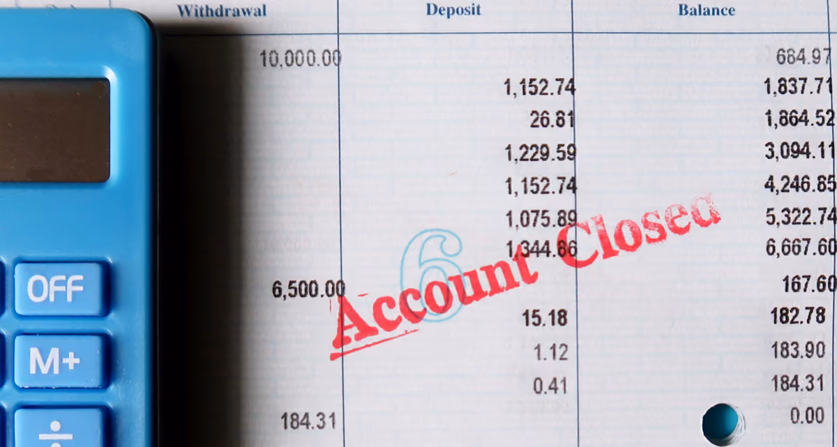 The edge of a calculator on top of a bank statement with "Account closed" stamped on it in red