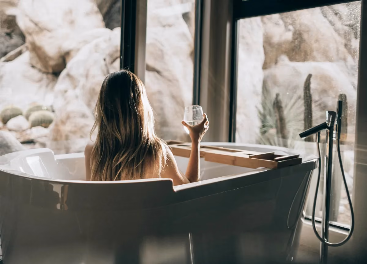 woman in white bathtub holding clear drinking glass