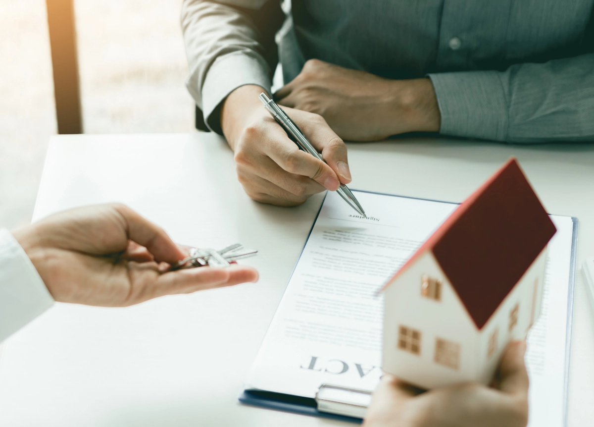 Client signing paper contract while real estate agent gives them a key