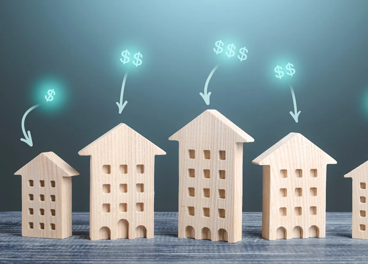 Dollar signs hovering above five wooden model houses