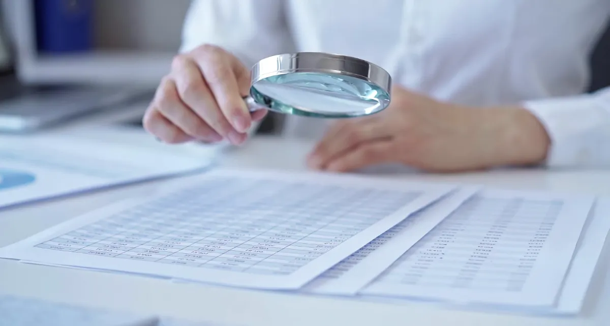 A person looking at a spreadsheet through a magnifying glass
