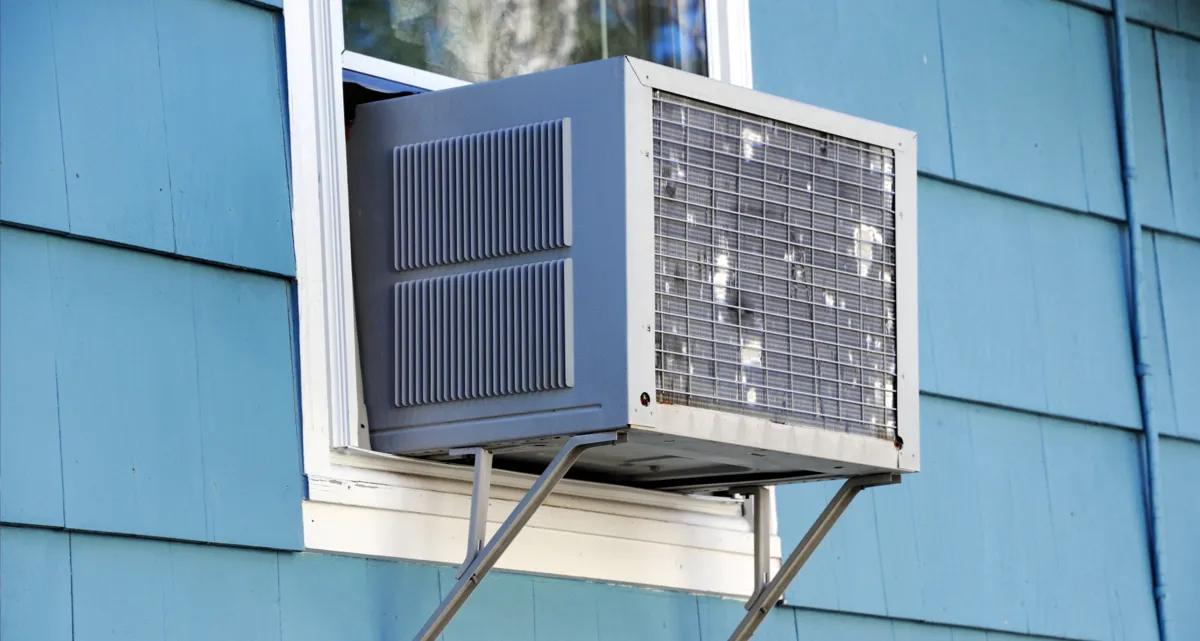 A window air conditioner unit on the side of a blue house