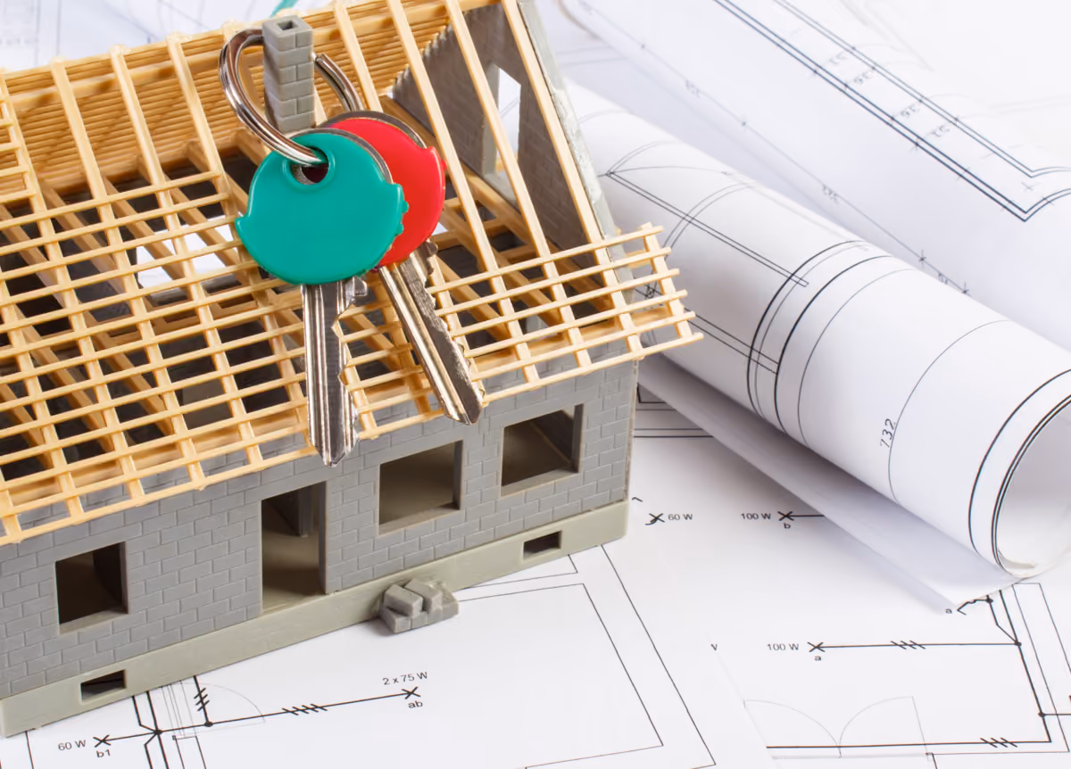 Small house under construction with home keys and rolls of diagrams and drawings for project