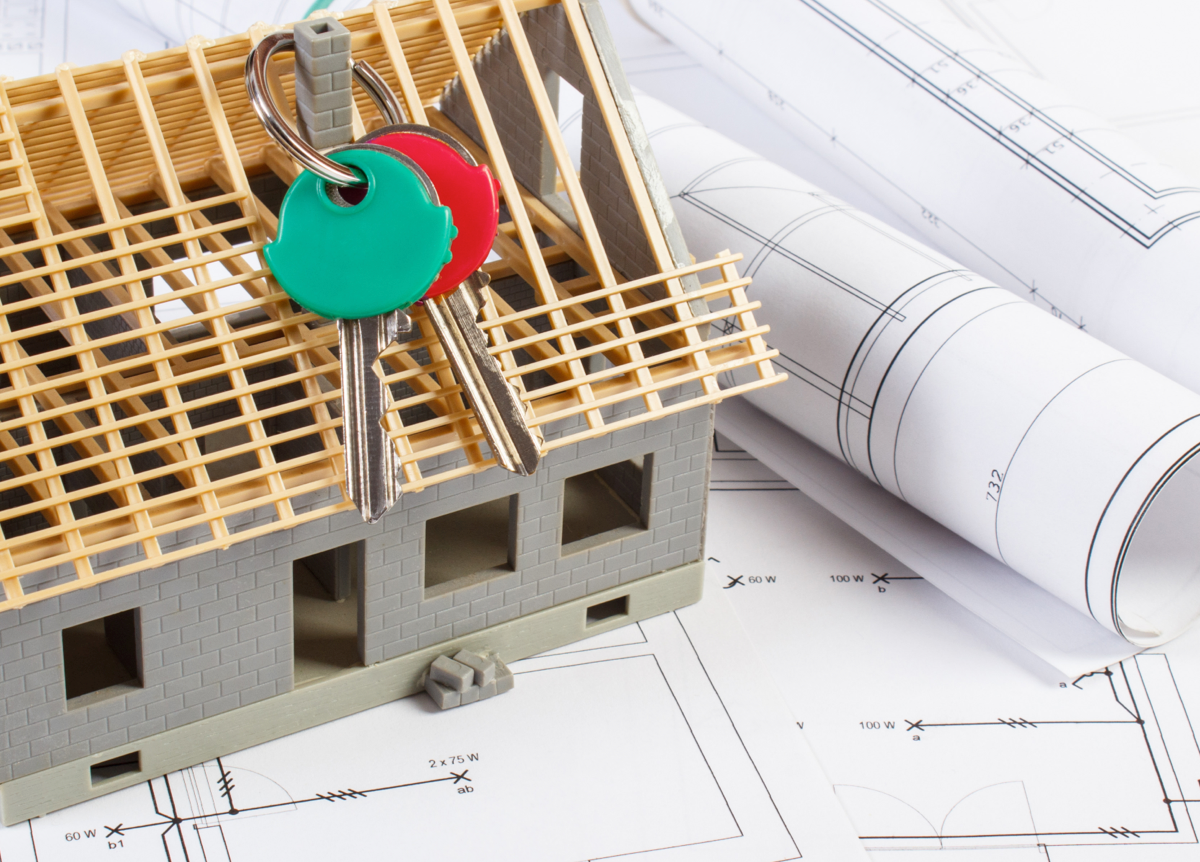 Small house under construction with home keys and rolls of diagrams and drawings for project