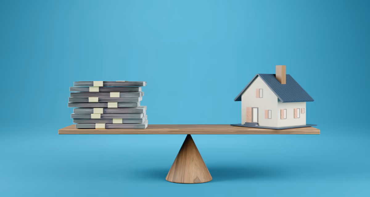 A model house and a stack of bank notes balancing on a scale