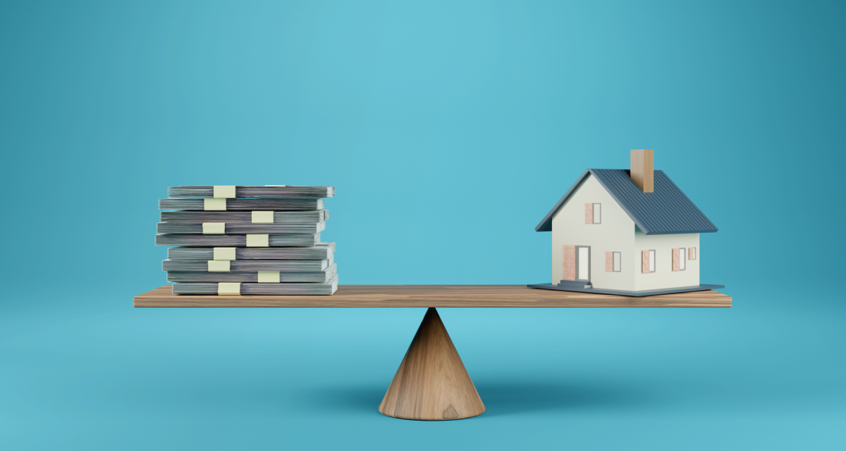 A model house and a stack of bank notes balancing on a scale