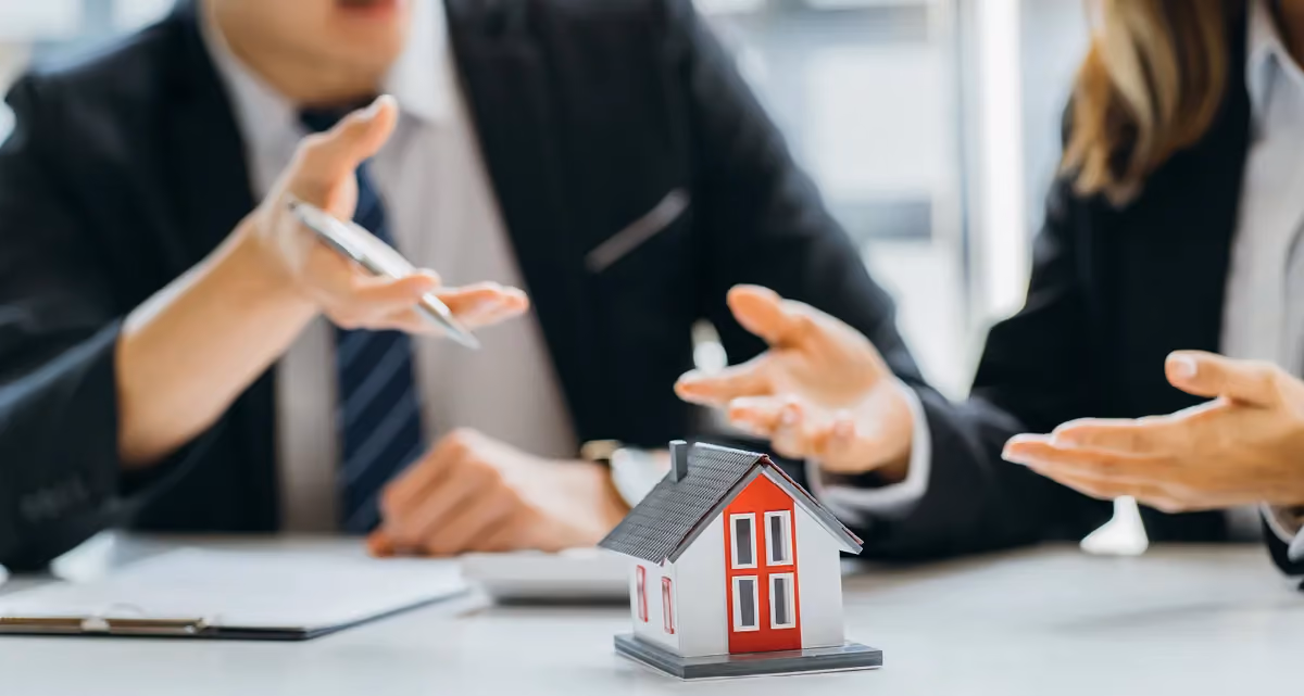 Two people in suits pointing at a model house