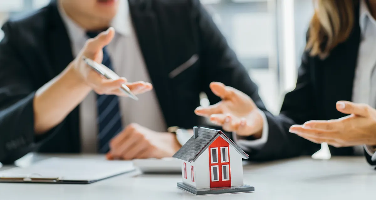 Two people in suits pointing at a model house