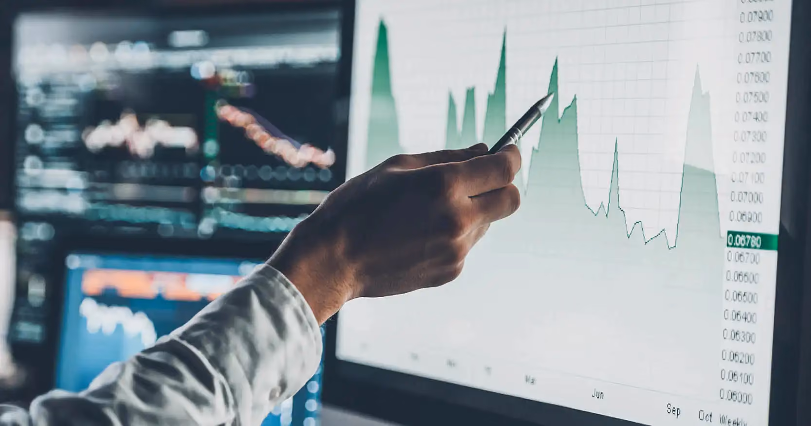 A man's hand using a pen to point at a graph on a computer screen