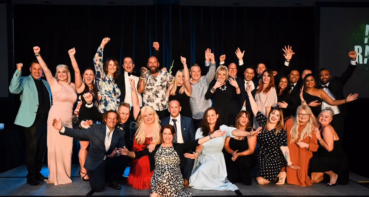 A group of joyous people celebrating on stage with their hands in the air