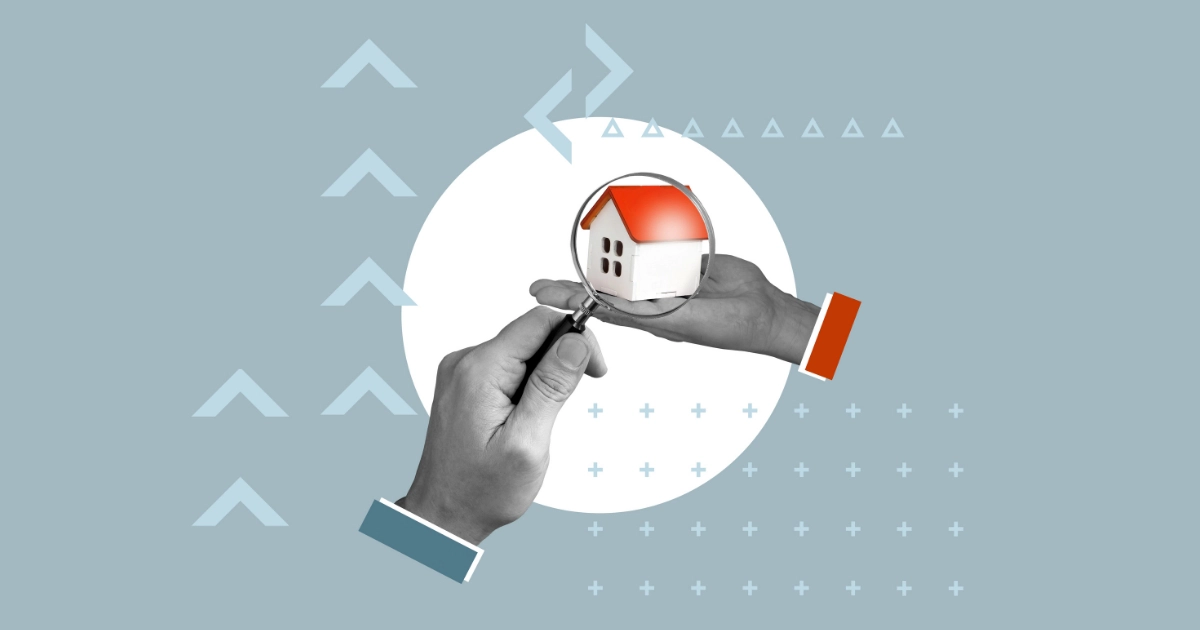 Two hands, one holding a model house and the other holding a magnifying glass