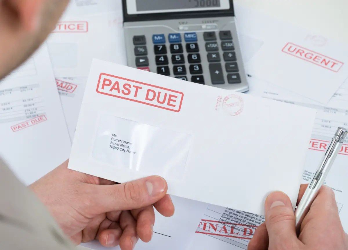 Man holding up one of several past due envelopes.