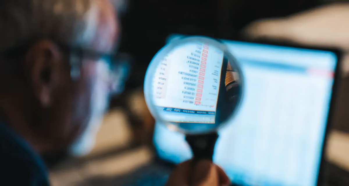 A man looking at a computer screen through a magnifying glass