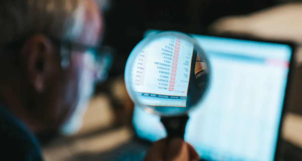 A man looking at a computer screen through a magnifying glass