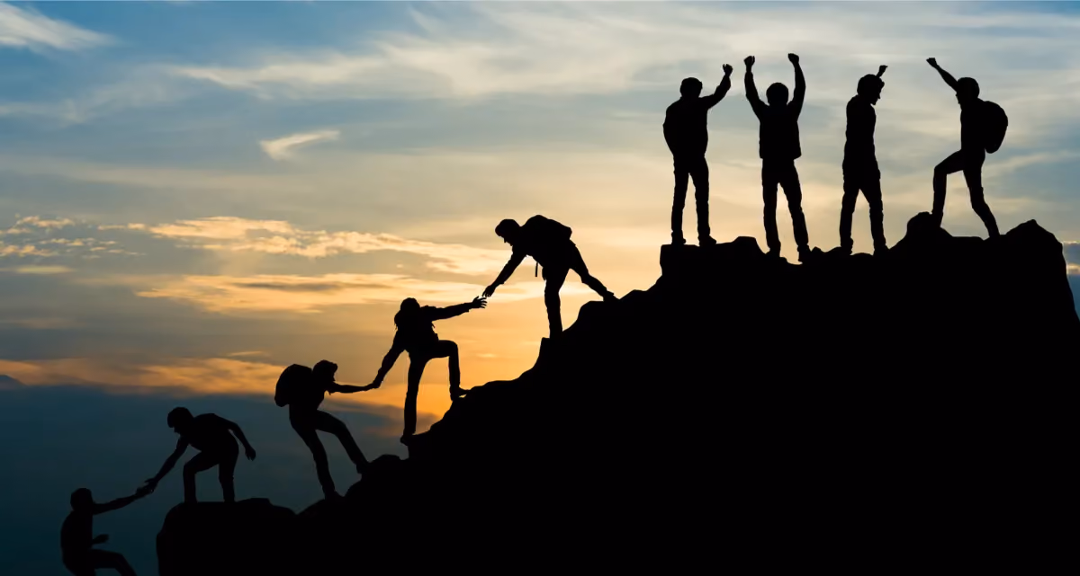 Silhouettes of eight climbers helping each other climb to a summit