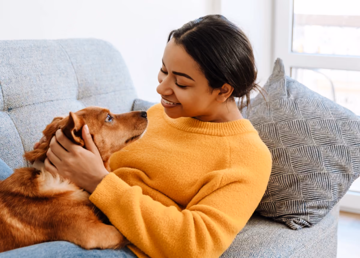 Young woman smiling and petting her dog while resting on couch