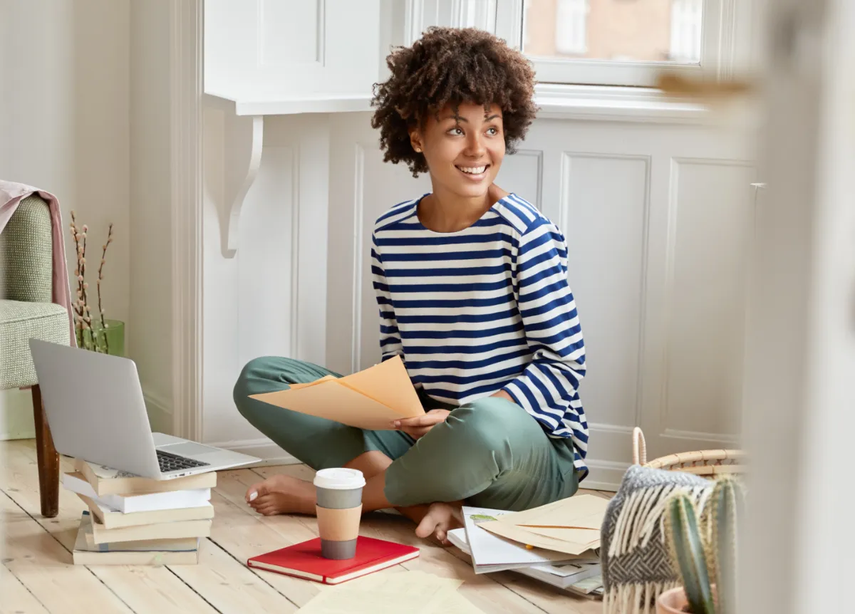 Young woman with books and laptop sitting on apartment floor